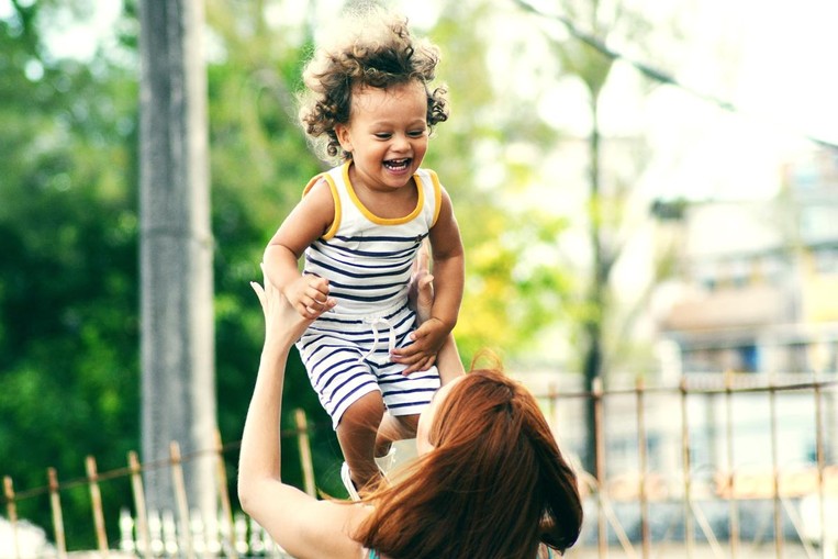 A mother holds up her child while smiling and laughing.