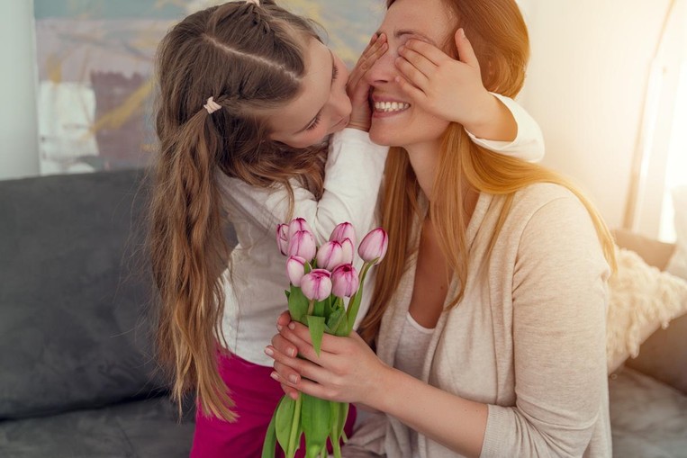 Little girl covering her mother's eyes while presenting her with a bouquet of flowers