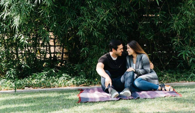 Couple sitting close together outside on a blanket, smiling.