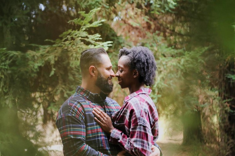 A man and woman get engaged and hold each other in a forest scene.