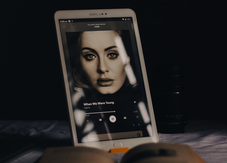 Ipad with Adele Spotify on the screen sitting next to book.