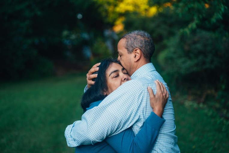 African American man and woman embrace with eyes closed.