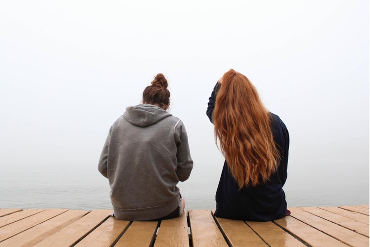 Two people sit next to each other on a dock looking into a foggy skyline.