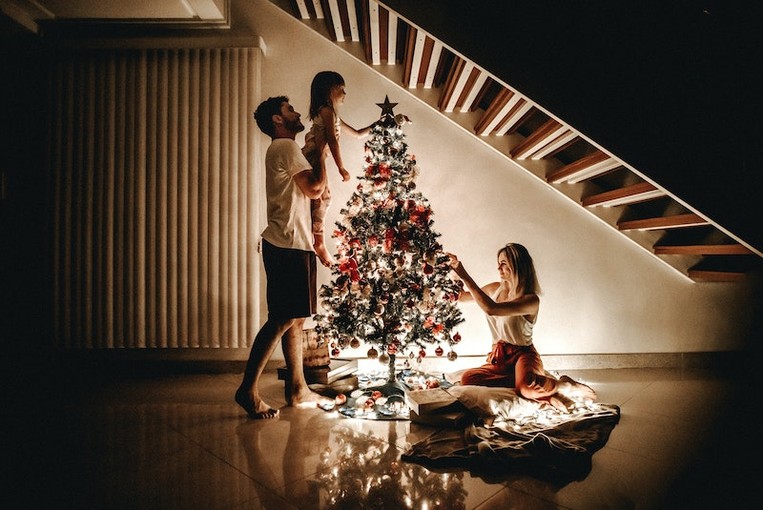 A man and a woman put ornaments on a Christmas tree with their child.