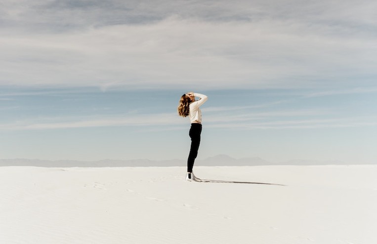 A girl stands alone in a desert.