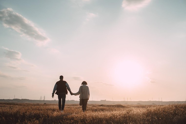 women and man walking towards sunset holding hands 