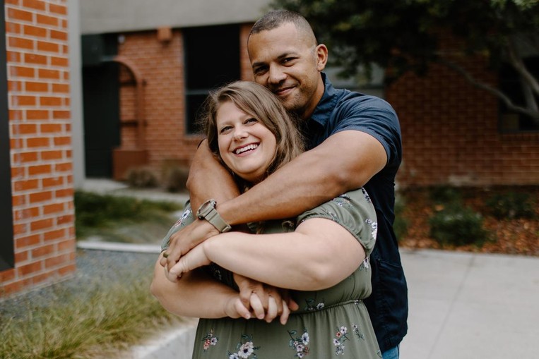 Husband hugging wife from behind, both simling 